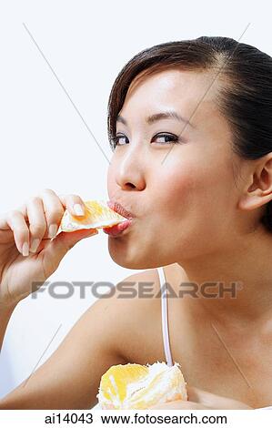 Stock Image - Woman eating orange, looking at camera. Fotosearch
