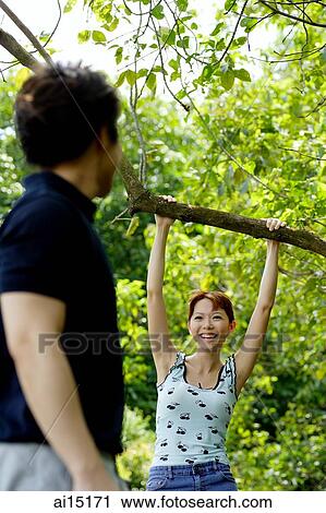 Woman hanging onto tree branch, looking at man across from her View Large Photo Image Stock Image - Woman hanging onto tree branch, looking at man across from her. Fotosearch