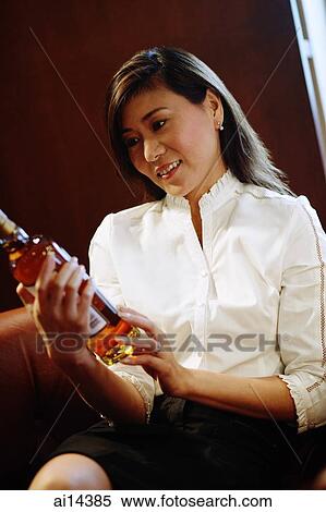 Woman holding and looking at alcohol bottle View Large Photo Image Stock Photography - Woman holding and looking at alcohol bottle. Fotosearch