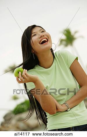 Stock Photo - Woman holding apple, laughing, looking away. Fotosearch