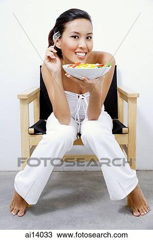 Stock Image - Woman holding bowl of salad, looking away. Fotosearch