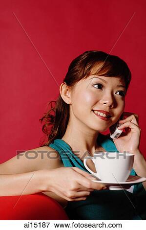 Woman holding cup and saucer, using mobile phone View Large Photo Image Stock Photo - Woman holding cup and saucer, using mobile phone. Fotosearch