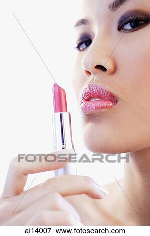 Stock Photo - Woman holding lipstick, looking at camera. Fotosearch