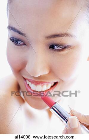 Stock Photo - Woman holding lipstick to lips, looking away. Fotosearch
