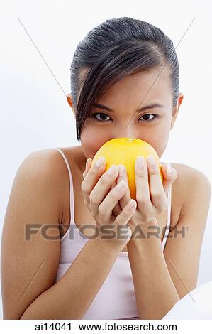 Stock Image - Woman holding orange to face. Fotosearch