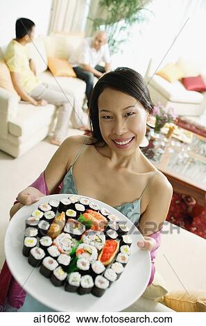 Woman holding up plate of sushi, looking at camera, people in the background View Large Photo Image Stock Image - Woman holding up plate of sushi, looking at camera, people in the background. Fotosearch