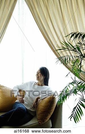 Woman in living room, sitting on sofa, looking away View Large Photo Image Stock Photo - Woman in living room, sitting on sofa, looking away. Fotosearch
