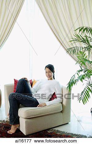 Woman in living room, sitting on sofa, smiling at camera View Large Photo Image Stock Photo - Woman in living room, sitting on sofa, smiling at camera. Fotosearch