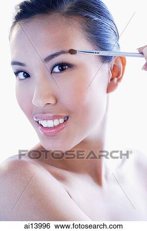 Stock Photograph - Woman looking at camera, using make-up brush. Fotosearch
