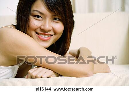 Woman lying on sofa, arms crossed, looking at camera View Large Photo Image Picture - Woman lying on sofa, arms crossed, looking at camera. Fotosearch