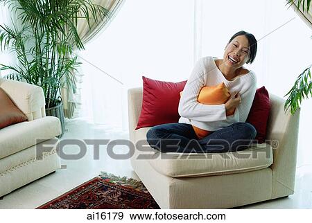 Woman sitting in living room, hugging pillow, smiling at camera View Large Photo Image Stock Photo - Woman sitting in living room, hugging pillow, smiling at camera. Fotosearch