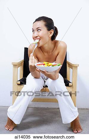 Stock Photography - Woman sitting on chair, holding bowl of salad, smiling at camera. Fotosearch