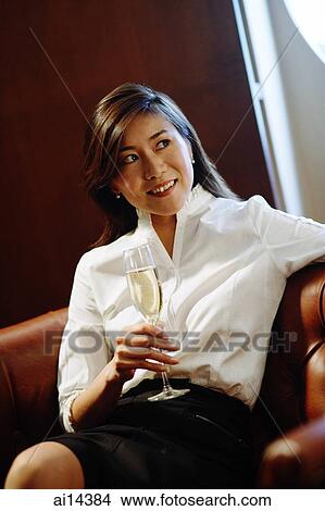 Woman sitting on sofa, holding glass on champagne, looking away View Large Photo Image Picture - Woman sitting on sofa, holding glass on champagne, looking away. Fotosearch