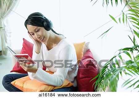 Woman sitting on sofa, wearing headphones View Large Photo Image Picture - Woman sitting on sofa, wearing headphones. Fotosearch