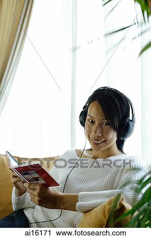 Woman sitting on sofa, wearing headphones, looking at camera View Large Photo Image Stock Image - Woman sitting on sofa, wearing headphones, looking at camera. Fotosearch