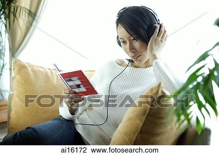 Woman sitting on sofa, wearing headphones, holding CD case View Large Photo Image Stock Image - Woman sitting on sofa, wearing headphones, holding CD case. Fotosearch