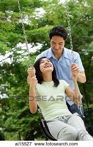 Woman sitting on swing, man behind her, pushing swing View Large Photo Image Stock Photo - Woman sitting on swing, man behind her, pushing swing. Fotosearch