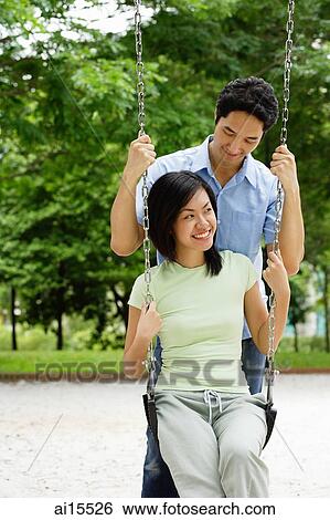 Woman sitting on swing, man behind her View Large Photo Image Stock Photograph - Woman sitting on swing, man behind her. Fotosearch