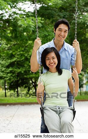 Woman sitting on swing, man behind her, smiling at camera View Large Photo Image Stock Photography - Woman sitting on swing, man behind her, smiling at camera. Fotosearch