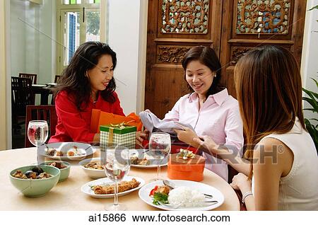 Stock Photograph - Woman sitting with friends unwrapping gifts. Fotosearch