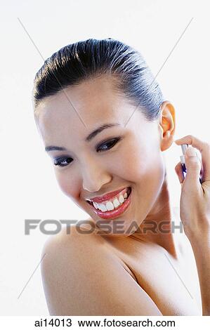 Stock Image - Woman spraying perfume, smiling. Fotosearch