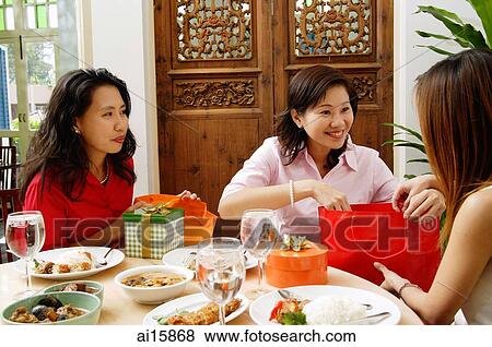 Stock Photo - Woman unwrapping gifts and looking at friend. Fotosearch