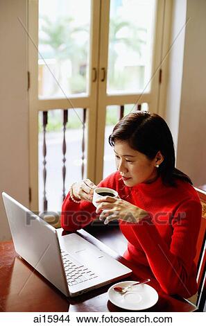 Woman using laptop, drinking from cup View Large Photo Image Picture - Woman using laptop, drinking from cup. Fotosearch