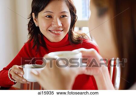 Stock Photography - Women holding cups, sitting face to face. Fotosearch