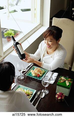 Stock Photography - Women in restaurant, food on the table, one woman holding bottle of wine. Fotosearch