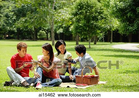 Stock Image - Young adults having picnic in park. Fotosearch