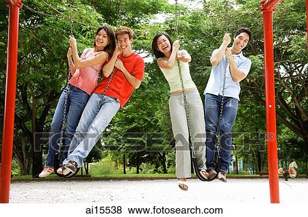 Young adults in playground, standing on swings, looking at camera View Large Photo Image Stock Photo - Young adults in playground, standing on swings, looking at camera. Fotosearch