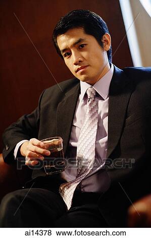 Stock Photo - Young businessman sitting on sofa, holding glass of whiskey. Fotosearch