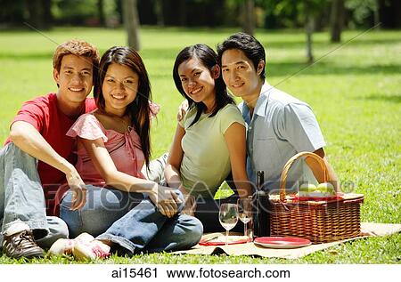 Stock Image - Young couples sitting in park, looking at camera, portrait. Fotosearch