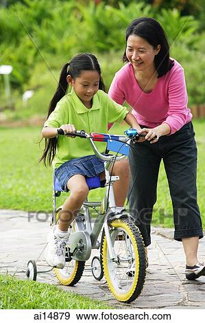 Young girl cycling, mother guiding her View Large Photo Image Stock Photo - Young girl cycling, mother guiding her. Fotosearch