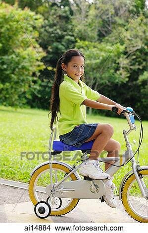 Picture - Young girl on bicycle, looking at camera. Fotosearch