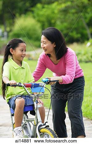 Young girl on bicycle, mother next to her View Large Photo Image Stock Image - Young girl on bicycle, mother next to her. Fotosearch