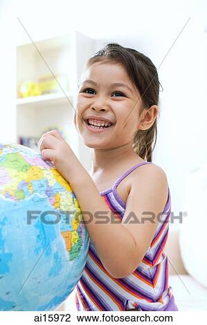 Stock Image - Young girl touching globe, smiling. Fotosearch