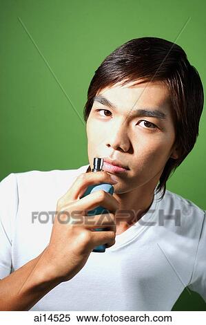 Young man holding bottle of perfume, looking at camera View Large Photo Image Stock Photography - Young man holding bottle of perfume, looking at camera. Fotosearch