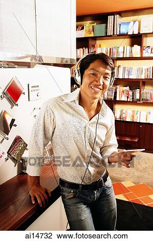 Young man listening to music, smiling, looking at camera View Large Photo Image Stock Image - Young man listening to music, smiling, looking at camera. Fotosearch