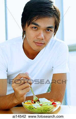 Young man looking at camera, bowl of salad in front of him View Large Photo Image Stock Image - Young man looking at camera, bowl of salad in front of him. Fotosearch