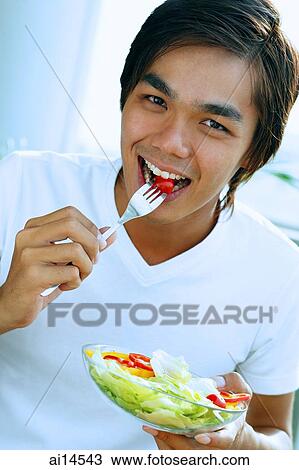 Young man looking at camera, eating salad View Large Photo Image Stock Image - Young man looking at camera, eating salad. Fotosearch
