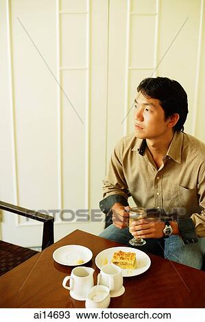 Young man sitting, holding coffee, looking away View Large Photo Image Stock Image - Young man sitting, holding coffee, looking away. Fotosearch