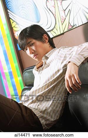 Young man sitting on sofa, looking at camera View Large Photo Image Stock Image - Young man sitting on sofa, looking at camera. Fotosearch