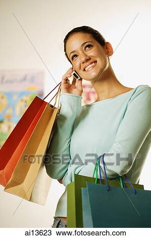 Young woman carrying shopping bags, using mobile phone View Large Photo Image Stock Image - Young woman carrying shopping bags, using mobile phone. Fotosearch