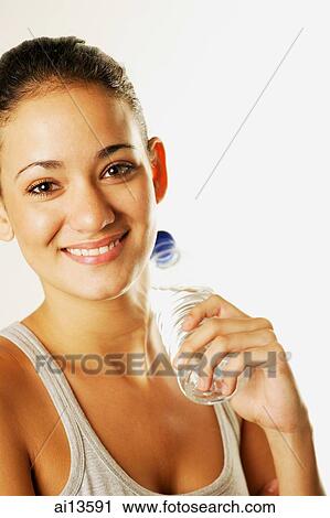 Stock Image - Young woman holding bottle of water, looking at camera. Fotosearch