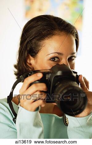 Young woman holding camera in front of her face View Large Photo Image Stock Photo - Young woman holding camera in front of her face. Fotosearch
