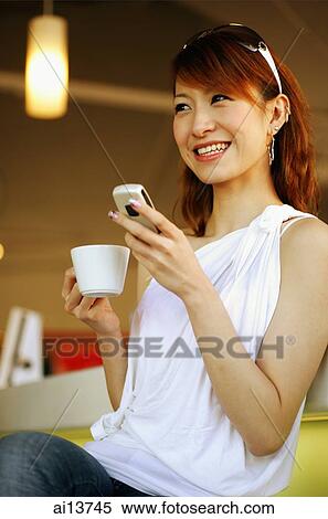 Young woman holding cup and mobile phone, smiling View Large Photo Image Stock Photography - Young woman holding cup and mobile phone, smiling. Fotosearch