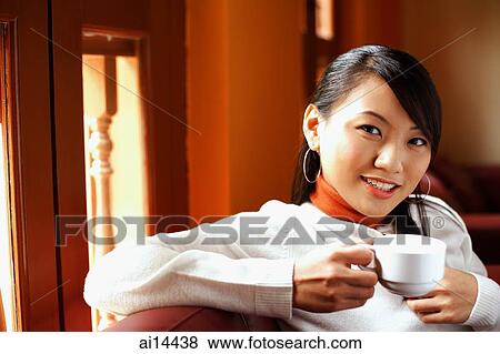 Stock Photo - Young woman holding cup, looking at camera. Fotosearch