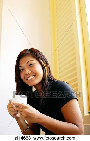 Young woman holding cup of coffee, looking at camera, smiling View Large Photo Image Stock Photo - Young woman holding cup of coffee, looking at camera, smiling. Fotosearch