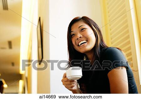 Young woman holding cup of coffee, looking away, smiling View Large Photo Image Stock Photo - Young woman holding cup of coffee, looking away, smiling. Fotosearch